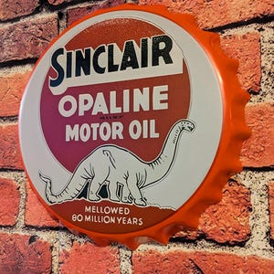 May include: A round, orange and white Sinclair Opaline Motor Oil sign. The sign features the Sinclair logo, the text "OPALINE MOTOR OIL", and a white dinosaur illustration. The sign is mounted on a brick wall.