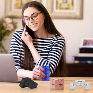 May include: A woman wearing glasses and a striped shirt is on a phone call. Several fidget toys in black, blue, rose gold, and silver are on the table. The toys are in various shapes and configurations.