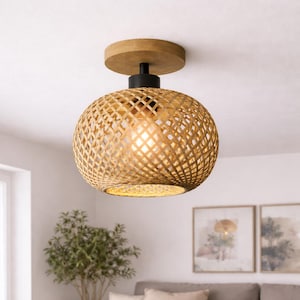Puede incluir: Una lámpara de techo empotrada de ratán tejido. La lámpara tiene una pantalla redonda tejida, una base de madera y un vástago negro. La luz está encendida, iluminando la pantalla tejida. El accesorio es de un color cálido y natural.