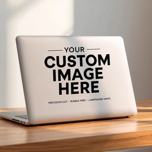 May include: A white laptop with the text "YOUR CUSTOM IMAGE HERE" is on a wooden table. A white mug and a small potted plant are also on the table. The laptop has the words "PRECISION CUT - BUBBLE-FREE - LAMINATED VINYL" below the main text.