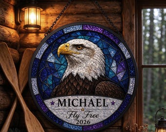 May include: A circular hanging sign featuring a stained glass style eagle portrait in shades of blue and purple. The sign includes the name MICHAEL, the phrase Fly Free, and the year 2026 printed on a white banner at the bottom with star accents.