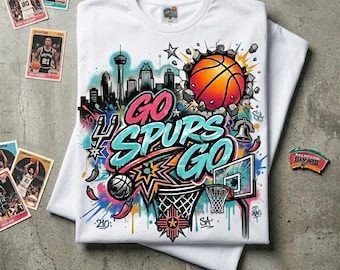 May include: White t-shirt with a vibrant graphic design. It features a basketball breaking through a wall, the text "GO SPURS GO", and a cityscape. Includes basketball trading cards and a team pin.