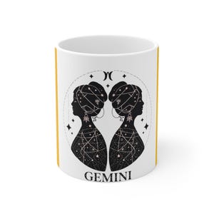 Puede incluir: Taza de cerámica blanca con asa y borde amarillos. La taza presenta una ilustración en blanco y negro de dos figuras femeninas silueteadas con diseños de estrellas y constelaciones, y la palabra "GEMINI" en la parte inferior.