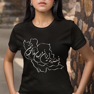 Puede incluir: Camiseta negra con un contorno blanco de una región geográfica y escritura estilizada. La camiseta de cuello redondo tiene un diseño sencillo. El diseño blanco está centrado en la parte delantera de la camiseta.