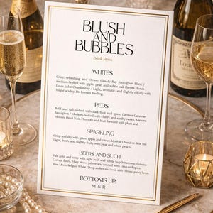 Può includere: Menu di bevande "Blush and Bubbles" con bordo dorato, che elenca vini, spumanti e birre. Sono visibili bottiglie e calici di champagne, candele e una penna. Il menu è su un tavolo.
