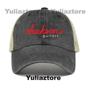 Pu&ograve; includere: Un cappellino da baseball grigio antracite con retro in rete beige e visiera curva. Il cappellino presenta il testo rosso "Jackson" in corsivo sopra la parola "guitars" in bianco. Un classico cappellino trucker.