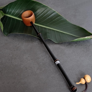 May include: A long-handled tea ladle featuring a natural light brown wooden cup and a slender, polished black handle. A small white tag with the number 252 is attached to the handle. A small, light-colored gourd-shaped charm hangs from the end.