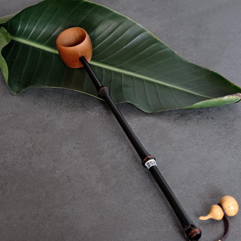 May include: A long-handled tea ladle featuring a natural light brown wooden cup and a slender, polished black handle. A small white tag with the number 252 is attached to the handle. A small, light-colored gourd-shaped charm hangs from the end.