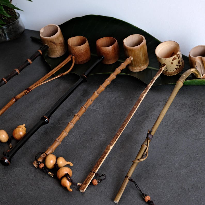 May include: A collection of six long-handled bamboo ladles with cylindrical cups. Each ladle features a unique handle design, including natural bamboo stalks, polished dark wood, and smooth light wood, some accented with small gourd charms.