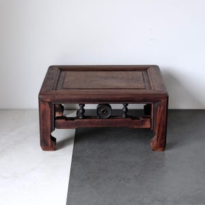 May include: A dark brown, rectangular wooden table with a raised border. The table has a decorative lower section with turned supports and a central, circular element. The legs are slightly curved. The table is likely antique or vintage.