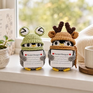 Puede incluir: Dos muñecos pingüinos de ganchillo sostienen tarjetas blancas con el texto: ❤️Pocket Penguin❤️ Here's a hug while I can't be there. Put me in your pocket and take me everywhere! Un pingüino lleva un gorro de rana, el otro un gorro de reno.
