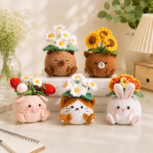 May include: Five crocheted animal figures serving as planters, each holding a different bouquet. The collection includes a brown bear with daisies, a brown bear with sunflowers, a pink pig with strawberries, a calico cat with daisies, and a white rabbit with orange flowers.