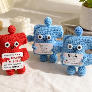 May include: Three handmade crochet figures in red and blue. The red figure holds a sign that reads "You were my missing piece and now it's you that makes me complete." The blue figures hold signs with text. One says "Never forget the difference." The other says "Mom I love you forever."
