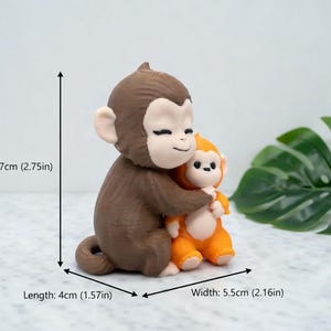 Pode incluir: Uma estatueta de macaco castanho e laranja, com 7 cm de altura, abra&ccedil;ando um macaco laranja menor. A estatueta tem 4 cm de comprimento e 5,5 cm de largura. Os macacos t&ecirc;m rostos sorridentes e est&atilde;o sobre um fundo claro.