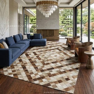 Könnte beinhalten: Ein großer rechteckiger Teppich mit einem geometrischen Patchwork-Muster aus quadratischen Fliesen in verschiedenen Braun-, Beige- und Cremetönen. Der Teppich liegt auf einem dunklen Holzboden in einem Raum mit einem blauen Ecksofa und Holzstühlen.