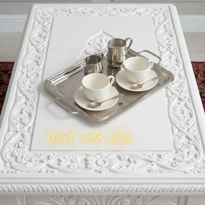 May include: A white ceramic mug with a black handle and the text "But First, Coffee" in a bold, black font. The mug is set against a blurred background, highlighting its clean design.