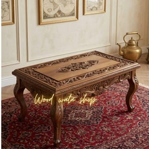May include: A rectangular, brown wooden coffee table with ornate carvings on the legs and tabletop. The table sits on a red patterned rug. The text "Wood wata shop" is visible on the table.