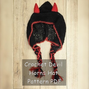 Puede incluir: Un gorro negro de ganchillo con ribetes y cuernos rojos, con dos trenzas. El sombrero tiene el texto "Crochet Devil Horns Hat Pattern PDF".