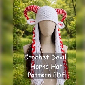 以下が含まれることがあります： 赤と白のストライプの角と、赤いアクセントが付いた長い白い三つ編みが付いた白いかぎ針編みの帽子。帽子は悪魔の角のデザインです。画像には「Crochet Devil Horns Hat Pattern PDF」と書かれています。