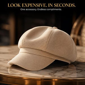 May include: A beige newsboy cap with a structured crown and a short, curved brim. The text at the top reads: LOOK EXPENSIVE. IN SECONDS. One accessory. Endless compliments. The cap features a soft, textured fabric finish and a central button detail.