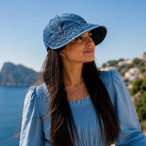 May include: A blue denim baseball cap with a wide, stitched brim and a distressed wash finish. The cap features a classic six-panel construction with a button top and a structured crown, providing a casual look with visible seam detailing.