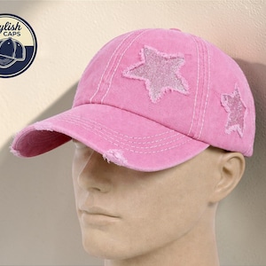 May include: A pink baseball cap with a distressed finish, featuring two star appliqués. The cap has a curved peak and a faded look. The logo for "Stylish Caps" is visible in the top left corner.