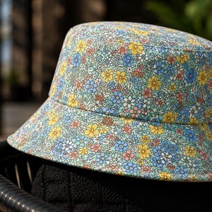 May include: A floral bucket hat with a light blue background and a pattern of small yellow, blue, and pink flowers. The hat is sitting on a black chair.