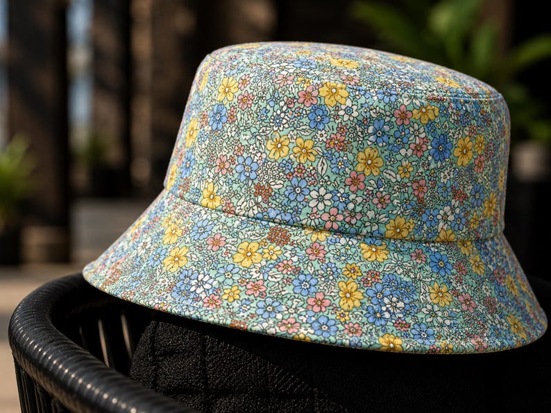 May include: A floral bucket hat with a light blue background and a pattern of small yellow, blue, and pink flowers. The hat is sitting on a black chair.