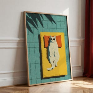 May include: A framed art print featuring a white cat wearing sunglasses, lounging on a yellow towel with an orange pillow. The background is a teal grid pattern, with shadows from a plant. The artwork is in a wooden frame.