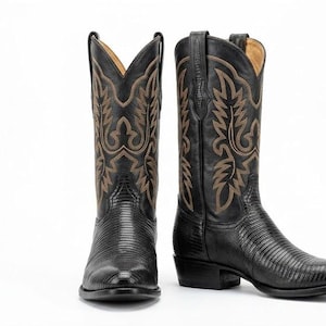 May include: A pair of black cowboy boots featuring a textured lizard-skin pattern on the foot and a tall shaft with intricate tan stitching in a flame-like design. The boots have a pointed toe, a stacked heel, and pull tabs at the top edges.
