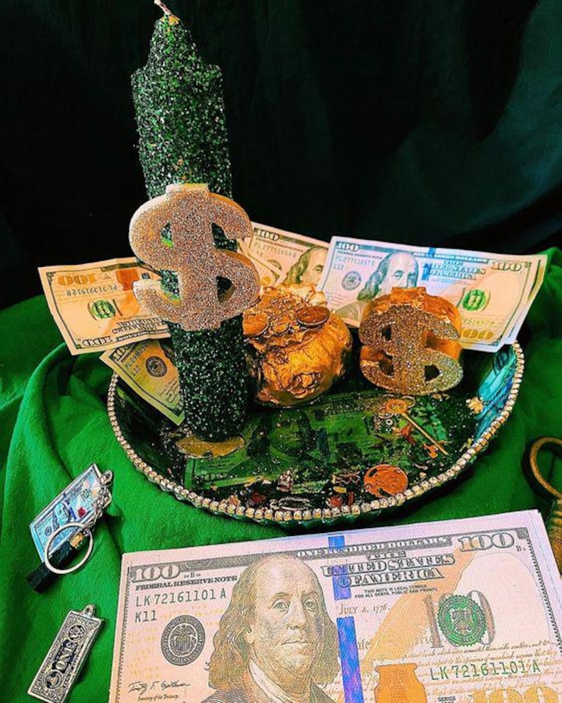 May include: A green glitter-covered candle with a gold dollar sign and a decorative tray filled with money and gold coins. Several $100 bills are visible, along with a keychain and a pendant.