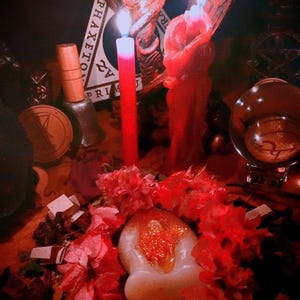 May include: A mystical scene with red and white candles, a crystal ball, and a decorative angel statue. The scene is illuminated by candlelight, with a focus on the ritualistic elements. The overall theme is spiritual and esoteric.