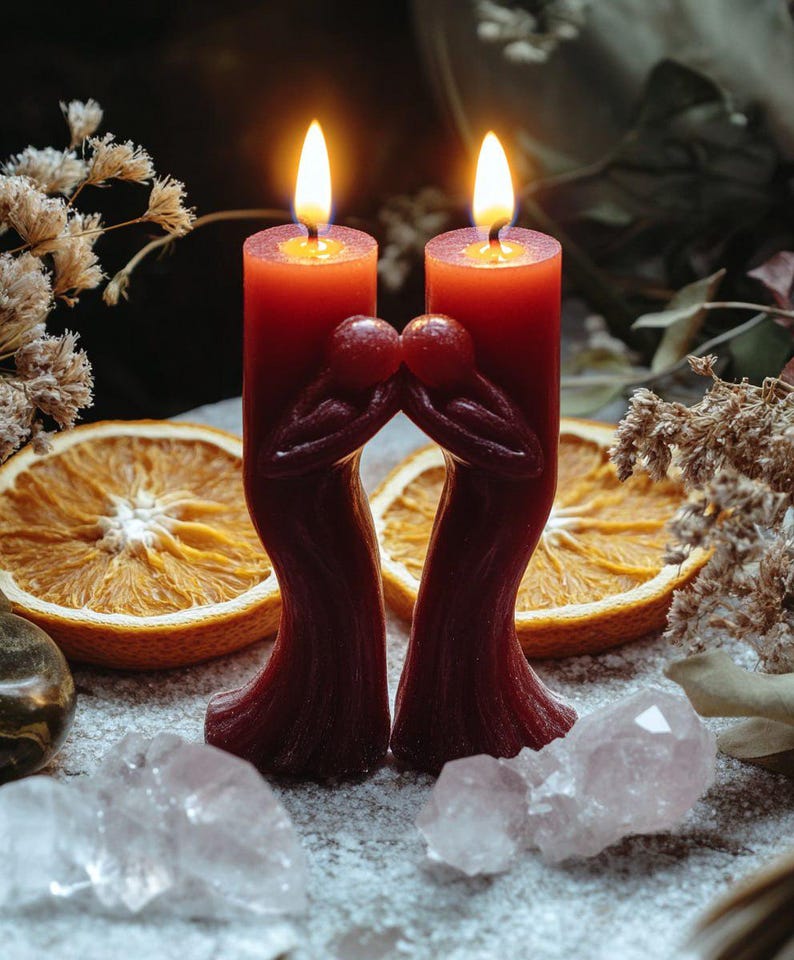 Pu&ograve; includere: Due candele a colonna rosse scure accese con un design unico di due figure che si abbracciano. Le candele sono circondate da fette d'arancia essiccate, cristalli e fiori secchi, creando un'atmosfera calda.