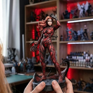 Puede incluir: Figura roja y negra de un personaje femenino con largo cabello rojo y un disfraz detallado. La figura se sostiene frente a una estantería llena de otras figuras. El personaje tiene garras afiladas y una pose dinámica.