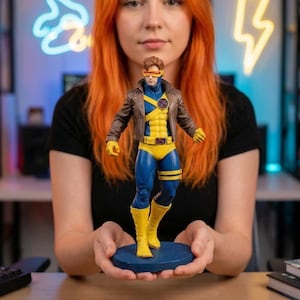 以下が含まれることがあります： 茶色のジャケット、黄色と青のスーツ、バイザーを特徴とするサイクロプスのアクションフィギュアが、青い台座に立っています。オレンジ色の髪の人の前にフィギュアが保持されています。背景にはネオンサインや他のフィギュアが含まれています。