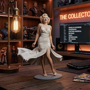 Puede incluir: Una figura detallada de Marilyn Monroe con un vestido blanco fluido, de pie sobre una base circular gris. La figura está sobre un escritorio de madera con una pantalla de computadora que muestra una lista de personajes. Una lámpara de estilo vintage y varias figuras de superhéroes están en el fondo.