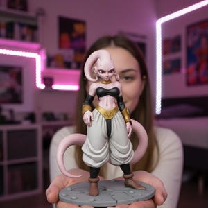 Puede incluir: Una figura rosa y blanca de un personaje con top negro, detalles dorados y pantalones blancos. La figura está sobre una base circular gris. El personaje tiene largos zarcillos rosas y es una representación estilizada.