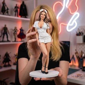 May include: A figurine of a woman in a white nurse's uniform, complete with a cap bearing a red cross. The figure is standing on a white circular base. The nurse is wearing black heels. The background includes other figurines and a neon sign.