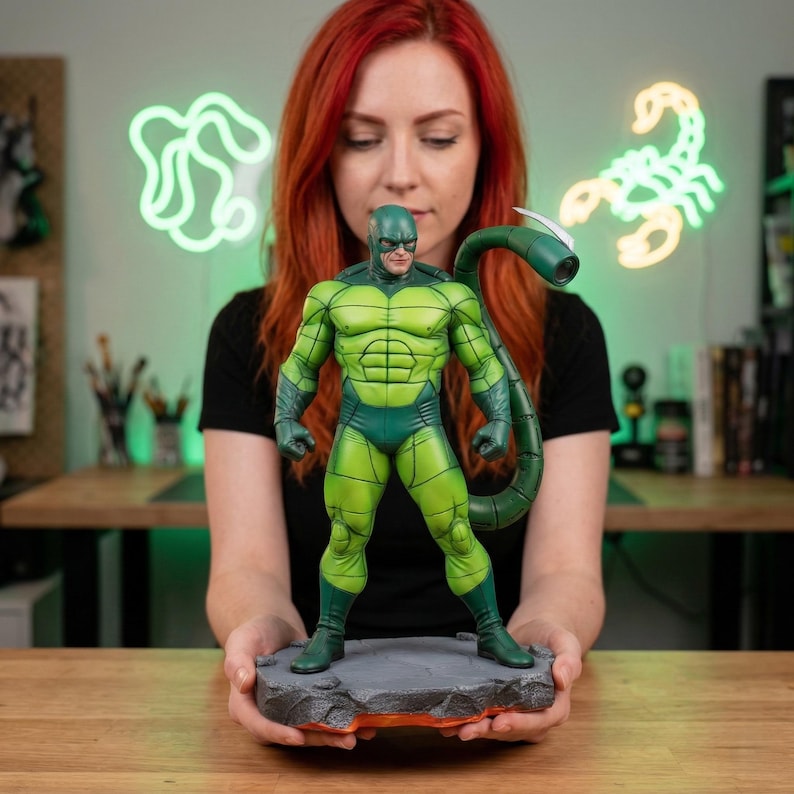 May include: A green and dark green Scorpion action figure. The figure is standing on a gray rock base with orange accents. The figure has a scorpion tail and is in a superhero pose.