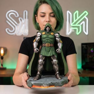 May include: A detailed statue of Doctor Doom, a Marvel Comics supervillain, is held up. The figure is clad in a green tunic and cape, with silver armour and a mask. The base is a rocky landscape with an orange glow.