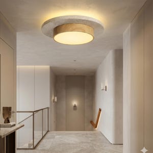 May include: A contemporary ceiling light with a circular design. It features a concrete-effect outer ring, a wooden central section, and a warm, bright light. The light is installed in a hallway with neutral walls and flooring.