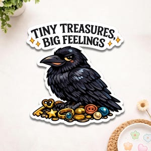 May include: A sticker featuring a cartoon crow with an intense expression, perched atop a pile of gold coins, keys, and buttons. The text "TINY TREASURES, BIG FEELINGS" is above the crow. The crow is black with yellow eyes.