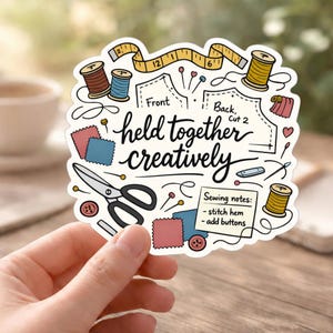 May include: A white sticker with a sewing theme, featuring spools of thread, scissors, fabric swatches, and a measuring tape. The text "held together creatively" is prominently displayed. Additional text includes "Sewing notes: - stitch hem - add buttons."