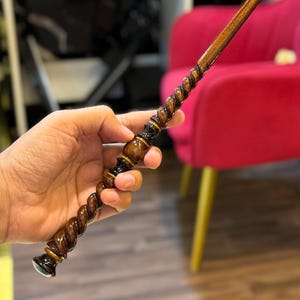 以下が含まれることがあります： 磨き上げられたダークブラウン仕上げの長く細い木製の杖。ハンドル部分は詳細な螺旋状のねじれデザインで、基部には滑らかで丸みを帯びた柄頭があり、先端に向かって真っ直ぐに細くなるシャフトが伸びています。