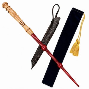 May include: A two-toned wand featuring a light brown wooden handle with carved rings and a smooth, glossy red shaft with two spherical accents. It is accompanied by a dark brown faux-reptile skin sheath and a long, navy blue velvet pouch with gold tassels.