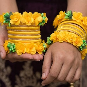 Könnte beinhalten: Gelbe Armreifen, verziert mit gelben Rosen und grünen Akzenten. Die Armreifen sind mit kleinen, funkelnden Verzierungen versehen. Das florale Design verleiht dem Schmuck einen Hauch von Eleganz.