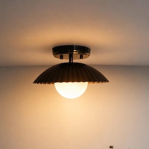 May include: A semi-flush mount ceiling light featuring a dark, ribbed, dome-shaped metal shade and a central spherical white glass globe. The fixture is mounted to the ceiling with a circular dark metal base, emitting a warm, soft glow.