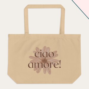 May include: Beige tote bag with long handles. The bag features a watercolour-style flower design in shades of brown, with the words "ciao amore!" printed in a dark brown font. The bag is made of a sturdy fabric.