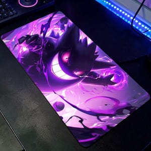Puede incluir: Alfombrilla de ratón rectangular con una ilustración morada y negra de un personaje de dibujos animados con una amplia sonrisa y ojos rosados brillantes. El diseño incluye efectos de energía morada arremolinada, creando una estética dinámica y vibrante.