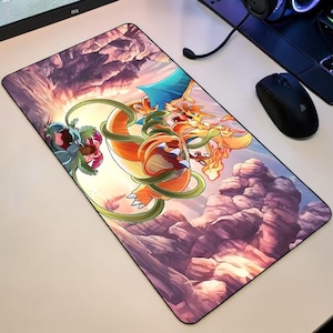 May include: A rectangular mousepad featuring a vibrant illustration of two fantasy creatures, one orange and the other blue and green, set against a mountainous landscape. The mousepad is designed for computer use and has a black border.